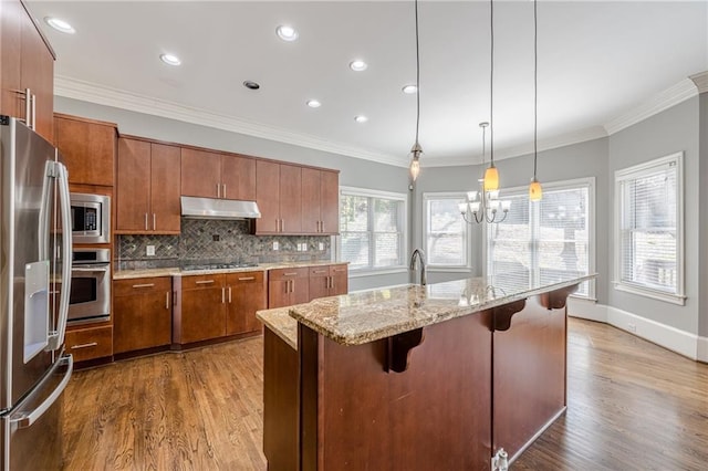 kitchen with decorative backsplash, brown cabinets, under cabinet range hood, and stainless steel appliances