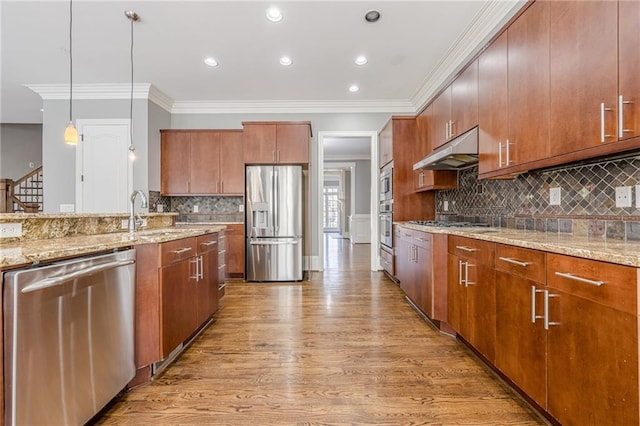 kitchen with a sink, light wood-style floors, under cabinet range hood, appliances with stainless steel finishes, and crown molding