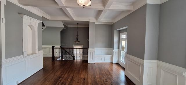 empty room with dark wood-type flooring, beamed ceiling, coffered ceiling, and wainscoting