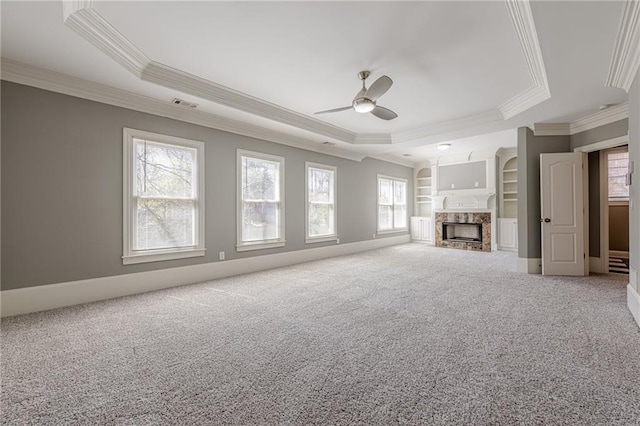 unfurnished living room with a tray ceiling, a healthy amount of sunlight, a premium fireplace, and carpet flooring