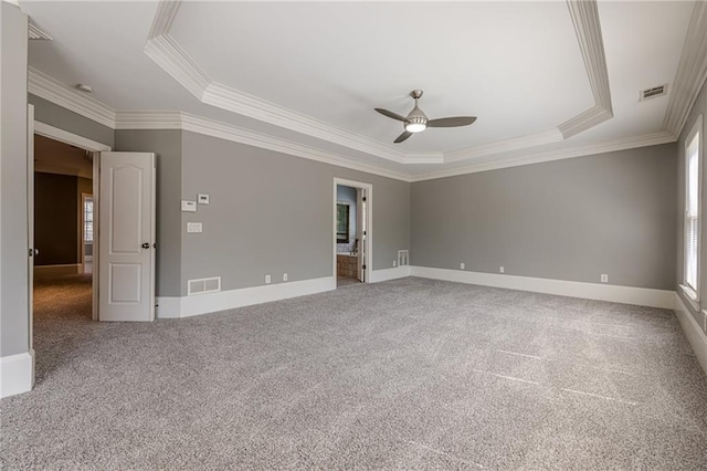 carpeted empty room featuring visible vents, a raised ceiling, baseboards, and ornamental molding