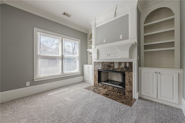 living room featuring built in shelves, visible vents, a premium fireplace, ornamental molding, and carpet flooring