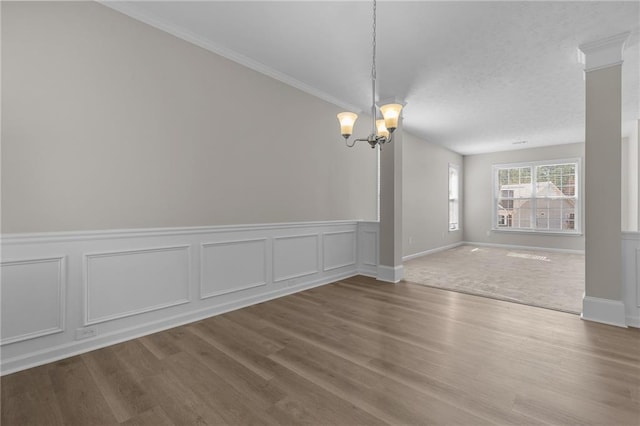 unfurnished room with an inviting chandelier, ornamental molding, wood finished floors, and wainscoting