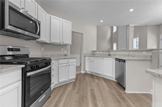 kitchen with white cabinets, light wood-style floors, stainless steel appliances, and a sink