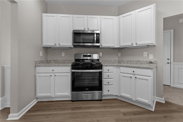 kitchen featuring appliances with stainless steel finishes, wood finished floors, light stone counters, and white cabinets