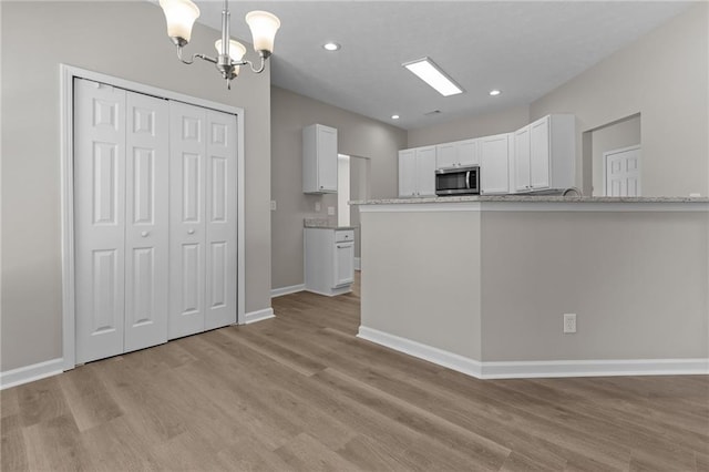 kitchen with light wood-style flooring, a notable chandelier, baseboards, white cabinets, and stainless steel microwave