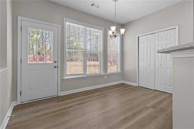 unfurnished dining area featuring a chandelier, wood finished floors, visible vents, and baseboards