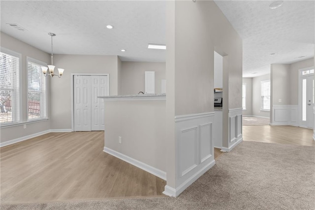 interior space featuring wainscoting, a textured ceiling, light wood-type flooring, a chandelier, and recessed lighting