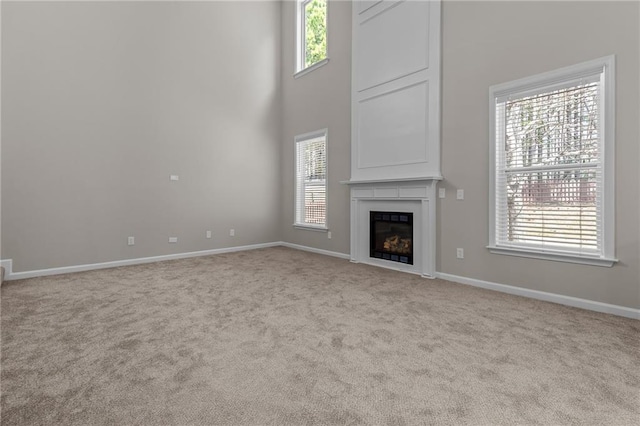 unfurnished living room featuring carpet floors, a high ceiling, a fireplace, and baseboards