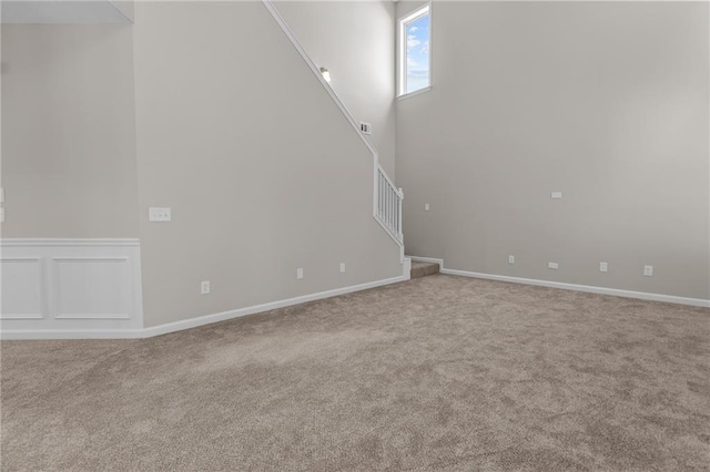 unfurnished living room featuring carpet, a high ceiling, and stairs