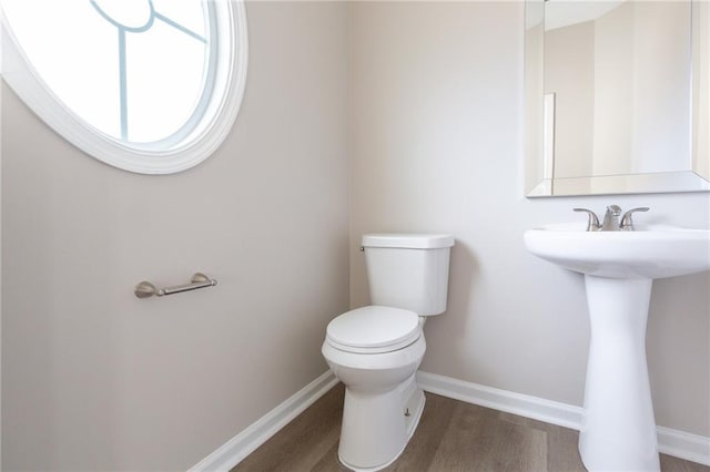 half bath with toilet, a sink, baseboards, and wood finished floors