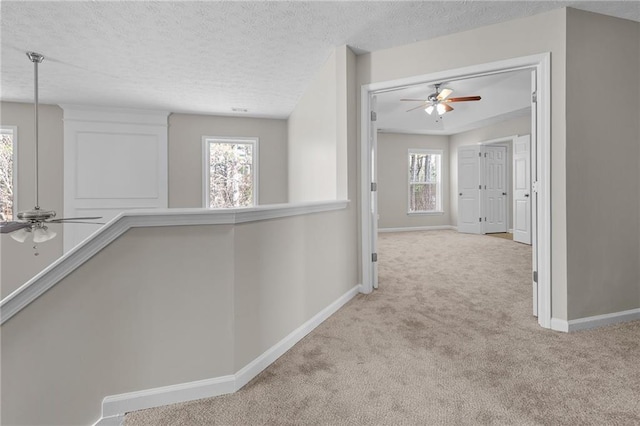 corridor with an upstairs landing, carpet flooring, a textured ceiling, and baseboards