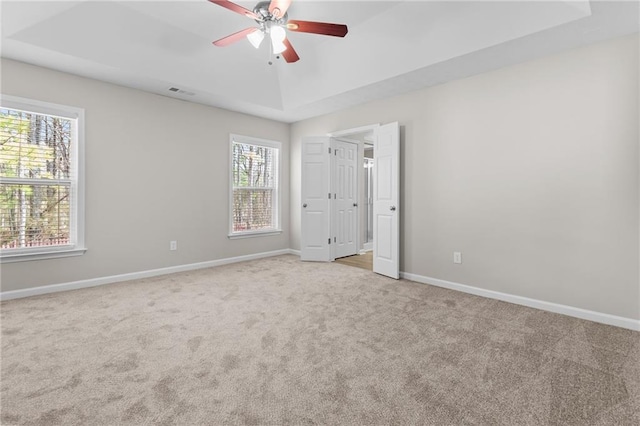 unfurnished bedroom featuring carpet floors, a ceiling fan, visible vents, baseboards, and a raised ceiling