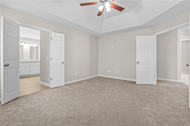 unfurnished bedroom featuring baseboards, a raised ceiling, and light colored carpet