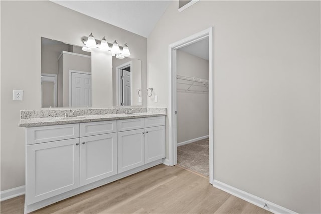 bathroom featuring lofted ceiling, double vanity, a sink, and wood finished floors