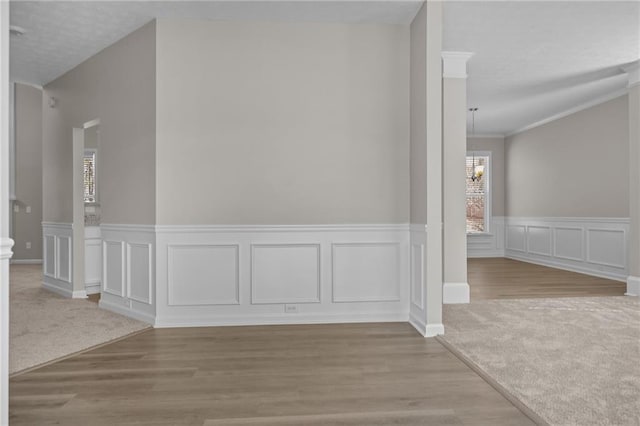 interior space featuring crown molding, a decorative wall, wood finished floors, and an inviting chandelier