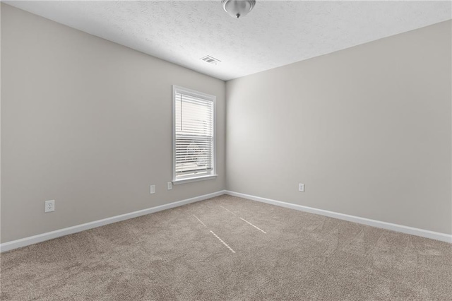 spare room featuring carpet floors, visible vents, a textured ceiling, and baseboards