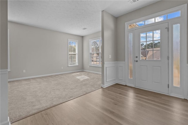 foyer entrance with a wainscoted wall, a textured ceiling, wood finished floors, and carpet flooring