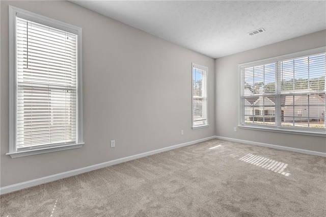 unfurnished room with a textured ceiling, carpet flooring, visible vents, and baseboards