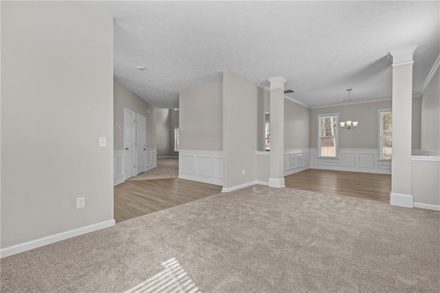 unfurnished living room featuring carpet floors, a wainscoted wall, a chandelier, and ornamental molding