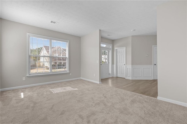 empty room with carpet flooring, visible vents, baseboards, and a textured ceiling