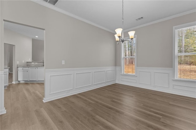 unfurnished dining area with crown molding, light wood-type flooring, visible vents, and a notable chandelier