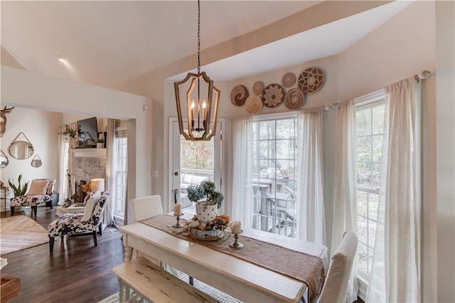 dining room featuring dark wood-type flooring, a chandelier, and a brick fireplace