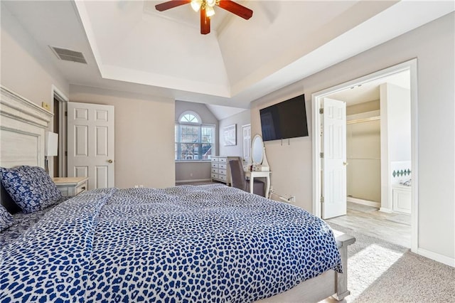 carpeted bedroom featuring a walk in closet, vaulted ceiling, ceiling fan, a tray ceiling, and a closet