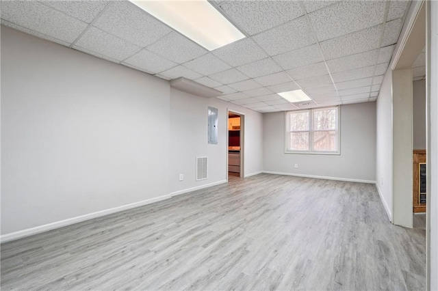 basement featuring a drop ceiling, light hardwood / wood-style floors, and electric panel