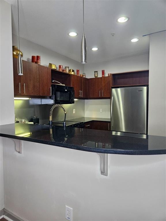 kitchen with a peninsula, freestanding refrigerator, black microwave, a kitchen breakfast bar, and decorative light fixtures