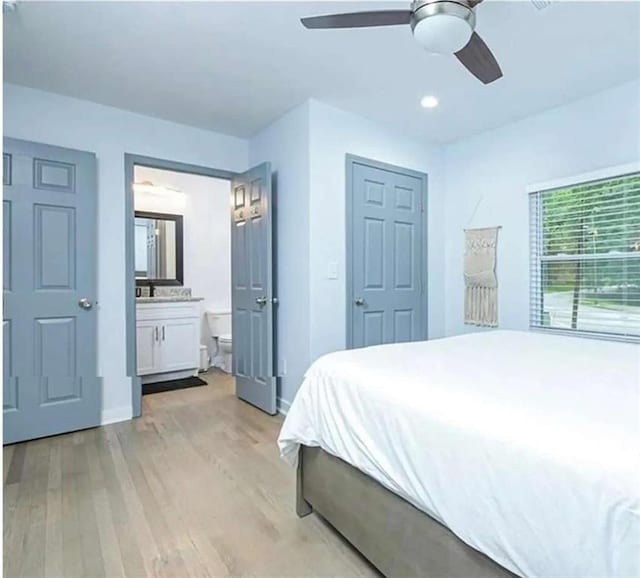 bedroom featuring ceiling fan, light wood-style flooring, baseboards, and ensuite bath