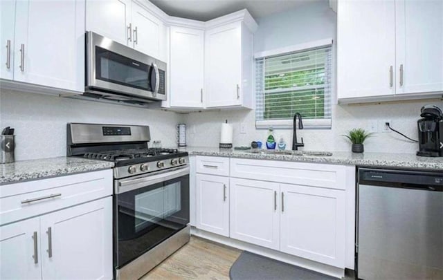 kitchen featuring light wood finished floors, appliances with stainless steel finishes, light stone counters, white cabinetry, and a sink