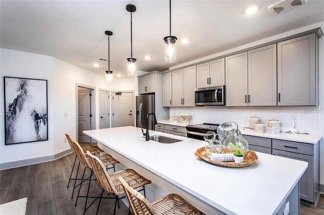 kitchen featuring gray cabinetry, sink, hanging light fixtures, a center island with sink, and appliances with stainless steel finishes