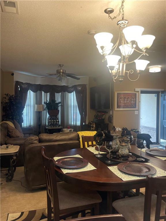 dining area with light colored carpet, visible vents, a wealth of natural light, and ceiling fan with notable chandelier