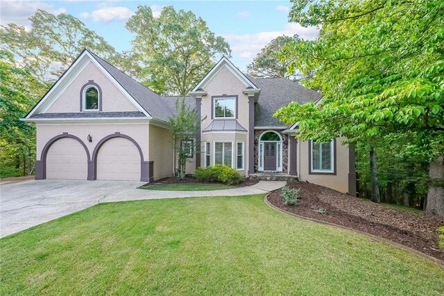 view of front of property with a shingled roof, a front lawn, stucco siding, and driveway