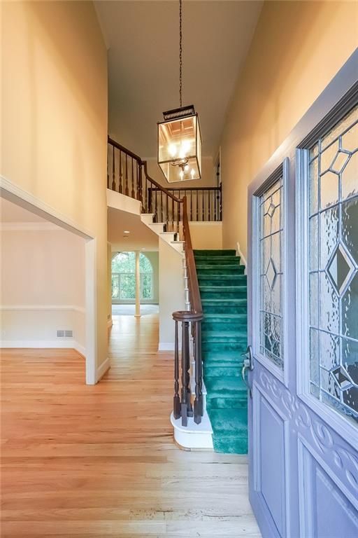 entrance foyer with visible vents, a towering ceiling, light wood-style floors, baseboards, and stairway