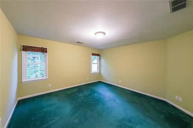 empty room featuring visible vents, baseboards, and dark colored carpet