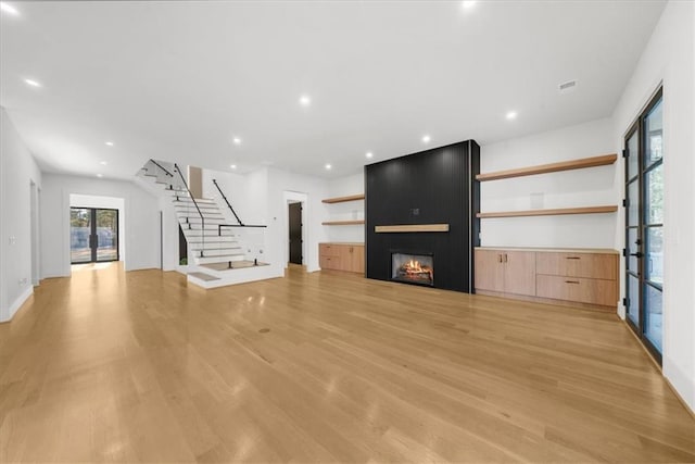 unfurnished living room featuring recessed lighting, light wood-style flooring, stairs, and a large fireplace