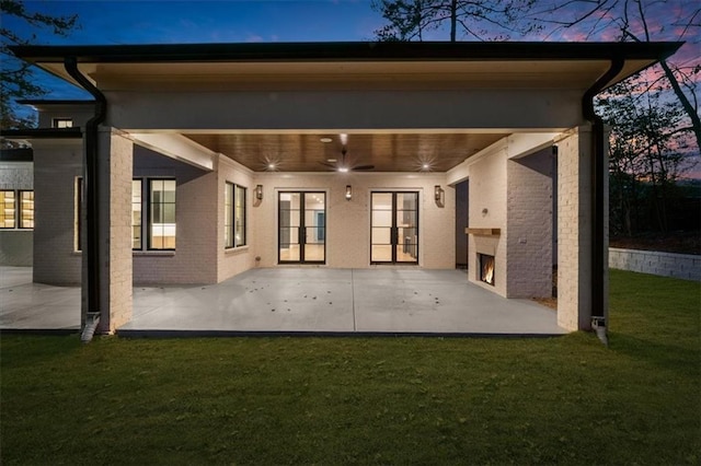 back of property with a patio area, a lawn, a warm lit fireplace, a ceiling fan, and brick siding