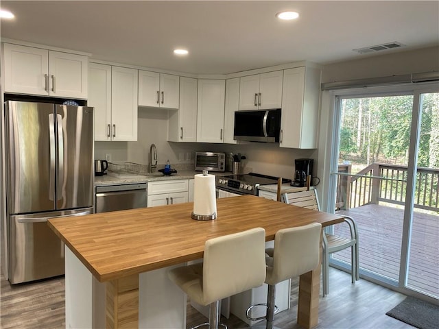 kitchen featuring stainless steel appliances, wooden counters, a kitchen island, and white cabinets