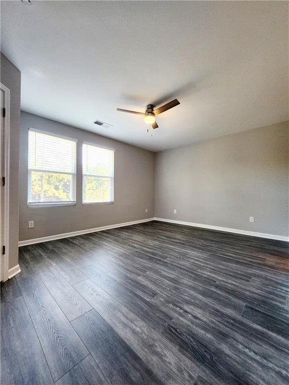 spare room with baseboards, visible vents, dark wood-style flooring, and ceiling fan