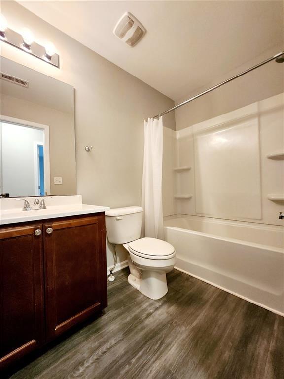 bathroom featuring visible vents, shower / bath combo with shower curtain, toilet, wood finished floors, and vanity