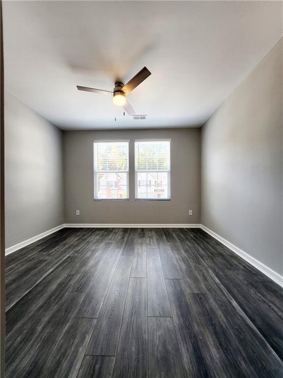 unfurnished room featuring visible vents, baseboards, a ceiling fan, and dark wood-style flooring