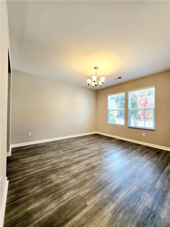 empty room featuring visible vents, baseboards, an inviting chandelier, and dark wood-style flooring