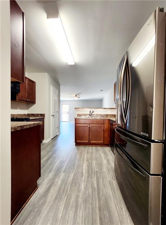 kitchen featuring baseboards, light wood-type flooring, a peninsula, freestanding refrigerator, and a sink