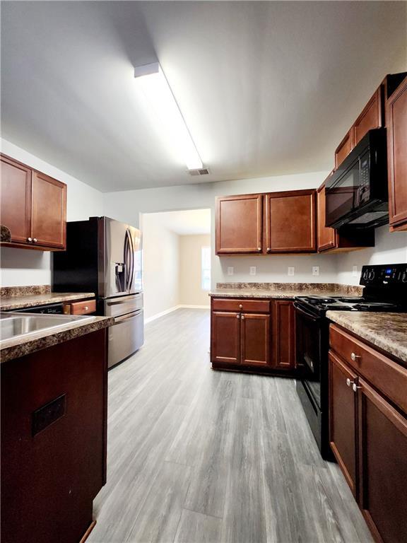 kitchen with visible vents, baseboards, black appliances, and light wood finished floors