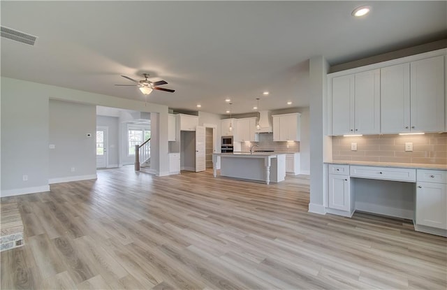 kitchen with premium range hood, a kitchen island with sink, white cabinets, ceiling fan, and appliances with stainless steel finishes