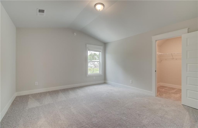 unfurnished bedroom with vaulted ceiling, light colored carpet, a spacious closet, and a closet