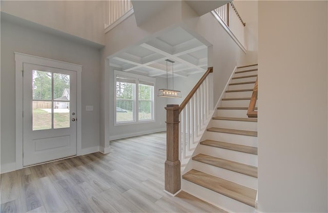 entryway with beam ceiling, light wood-type flooring, coffered ceiling, and a healthy amount of sunlight