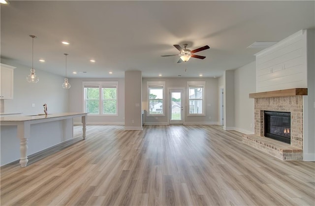 unfurnished living room with ceiling fan, light wood-type flooring, and a fireplace